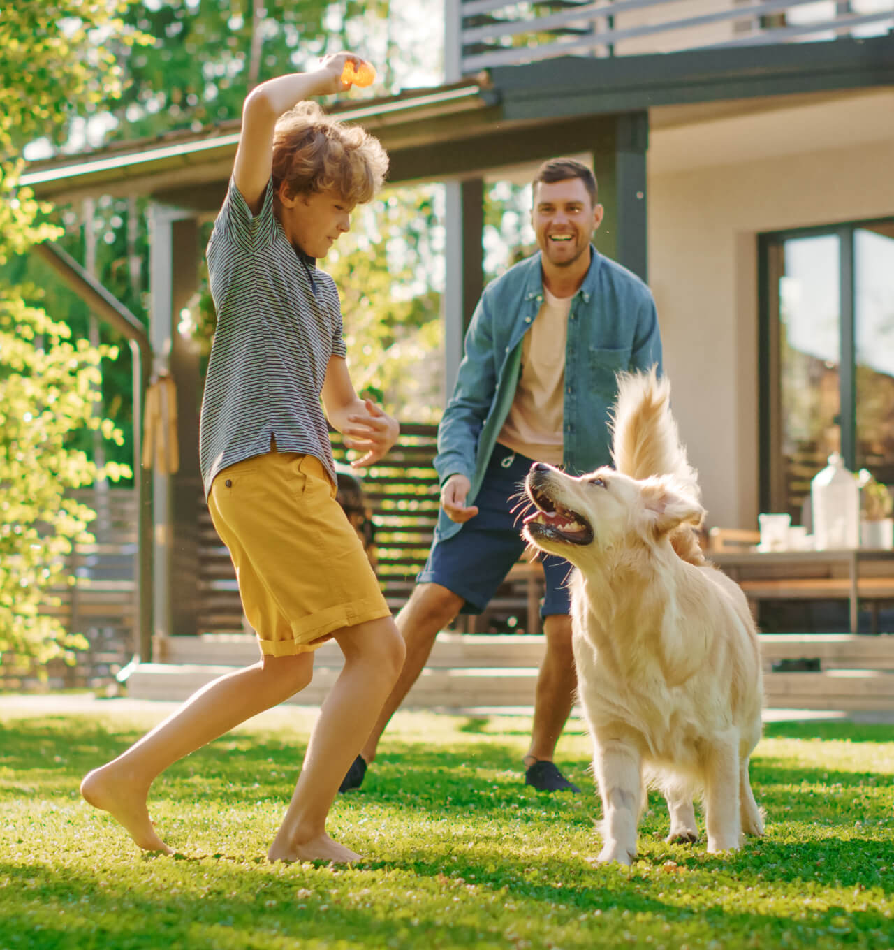 Young father and son playing with dog in back yard