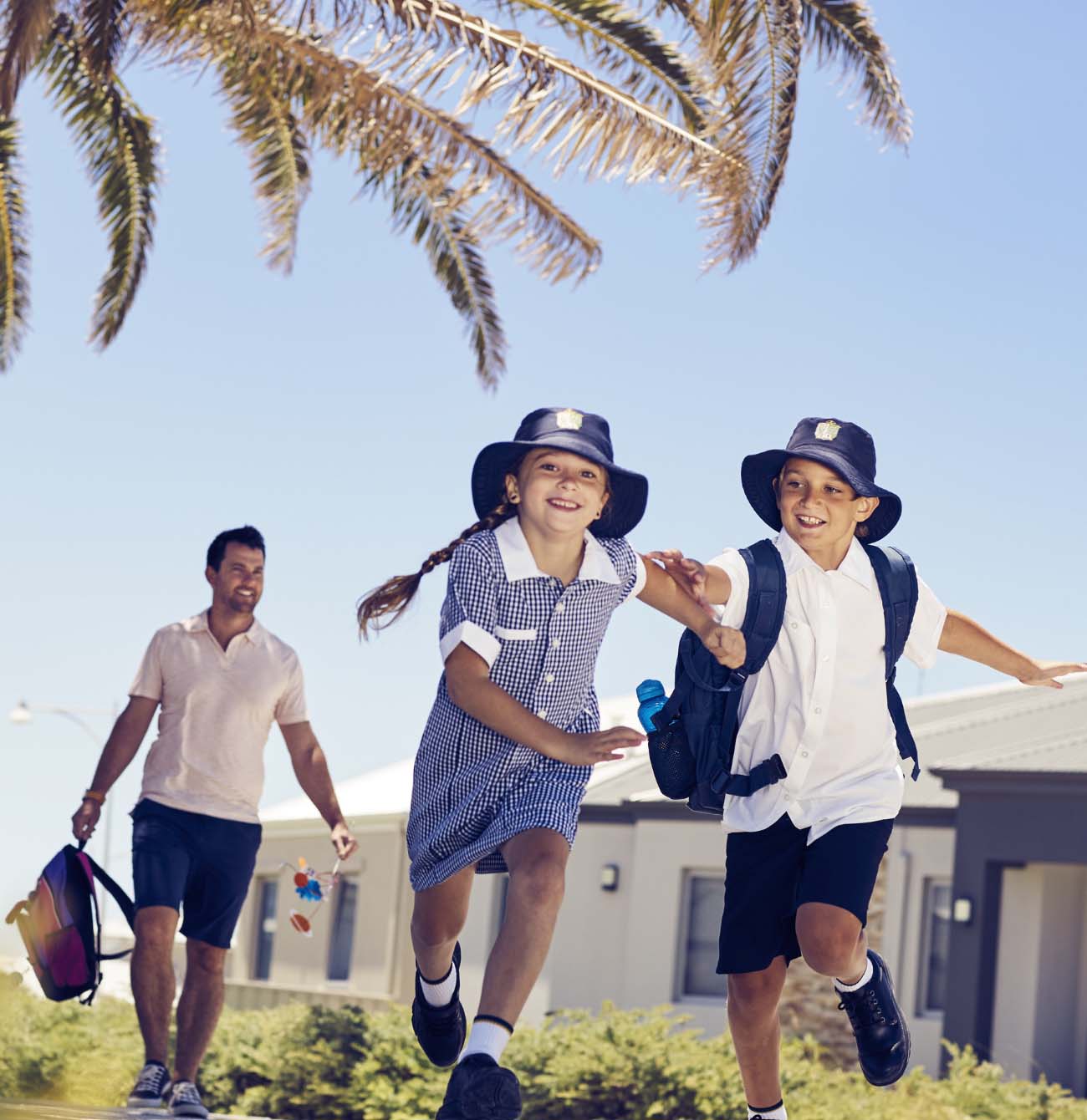 Primary aged children running to school with their father walking behind them