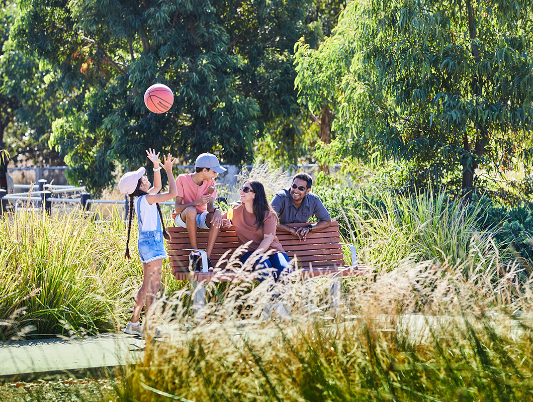 Maple Grove, Pakenham young family sitting on the park bench, with the young girl throwing a basketball in the air.
