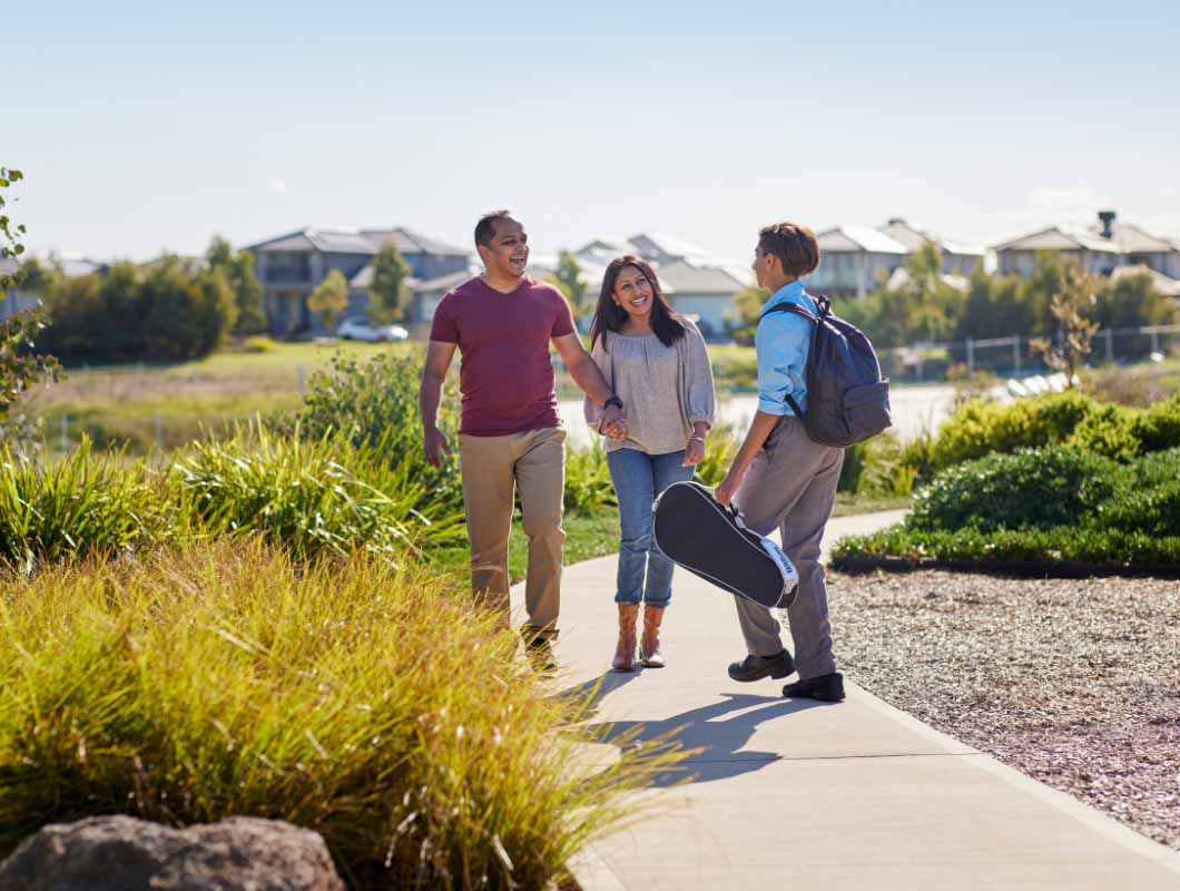 True North, Greenvale young family father, mother and son in school uniform, holding an instrument case, all walking along the footpath.