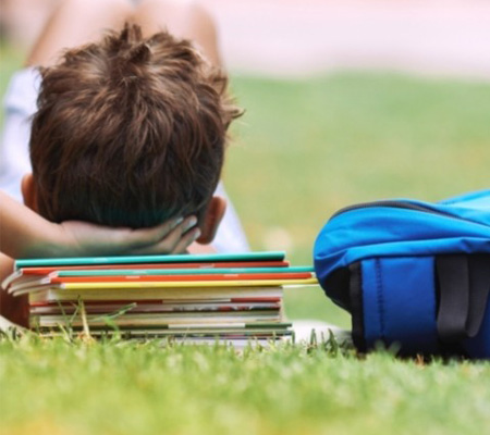 School boy relaxing on the lawn with his head on a pile of books in Allara, Eglinton.