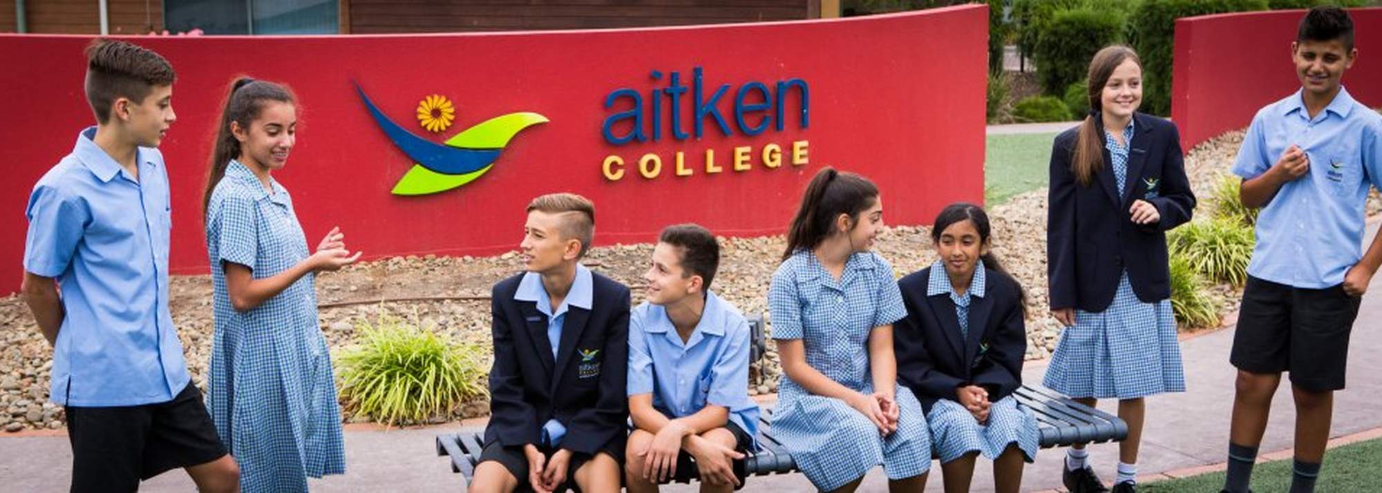 True North, Greenvale Aitken College students sitting in front of school entrance sign.