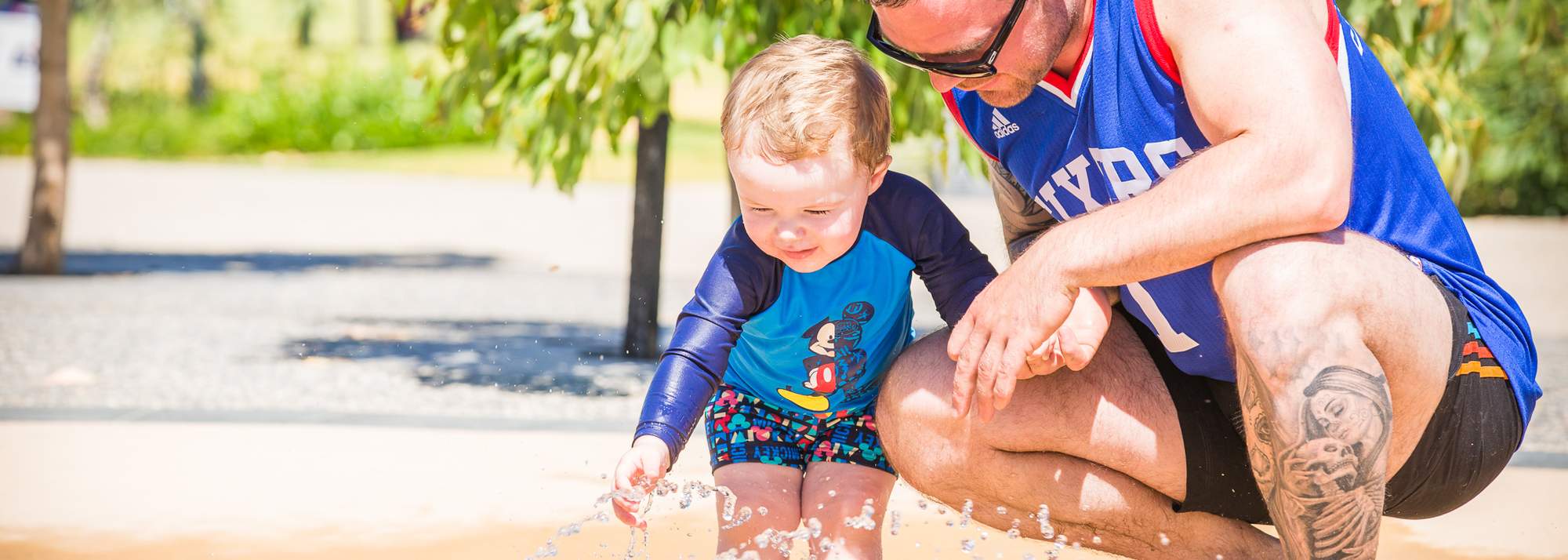 Allara, Eglinton Revolution playground, waterplay. Toddler with father enjoying the waterplay.