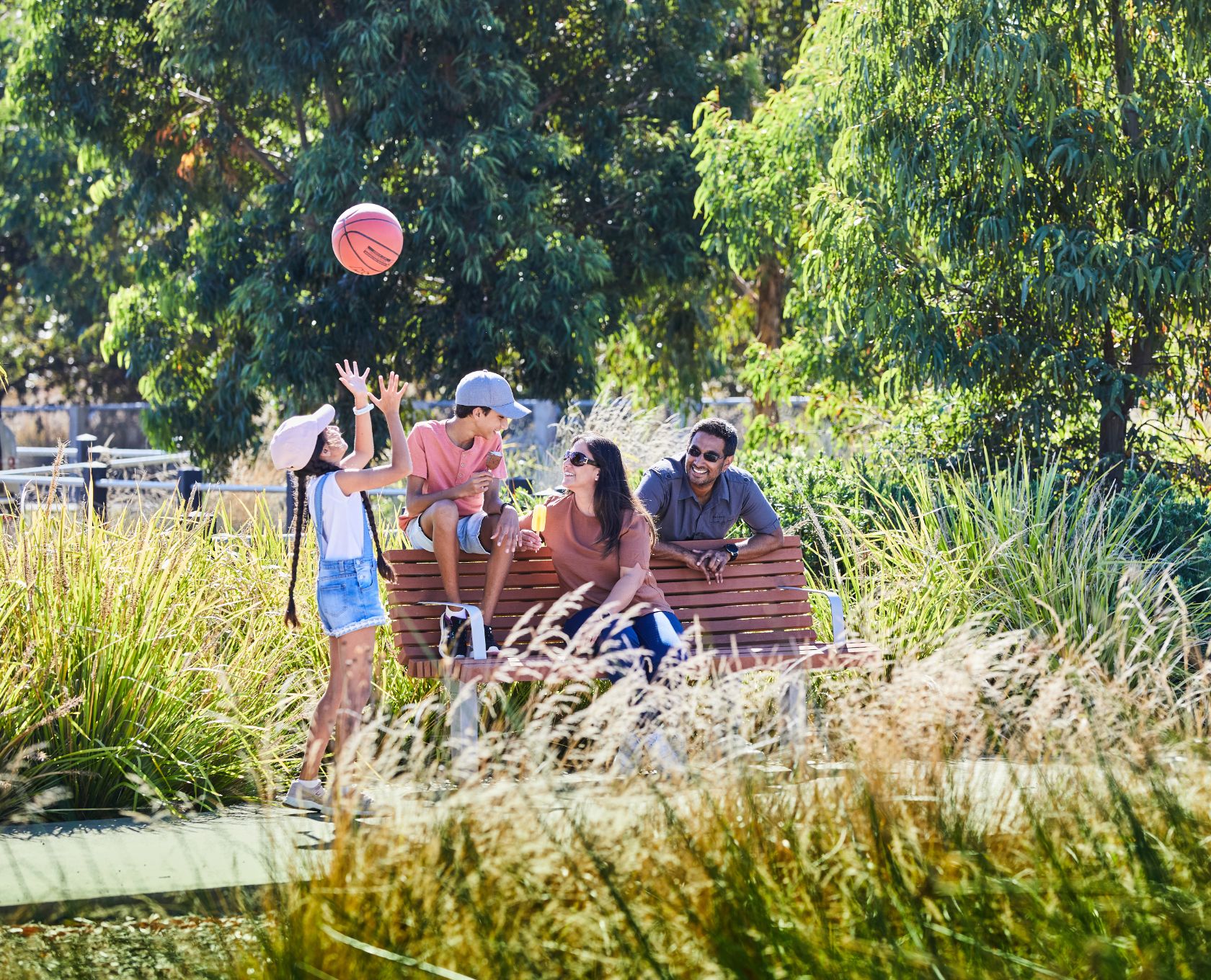 Maple Grove, Pakenham young family sitting on park bench, young girl throwing basketball up in the air.